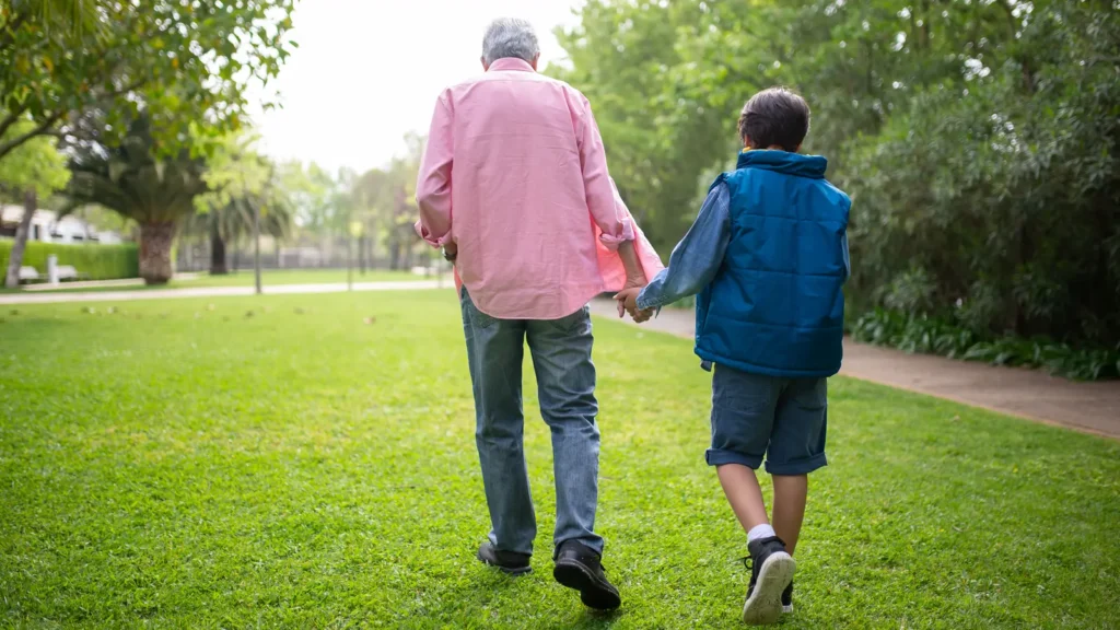 Grandfather and grandson walking hand in hand through a park