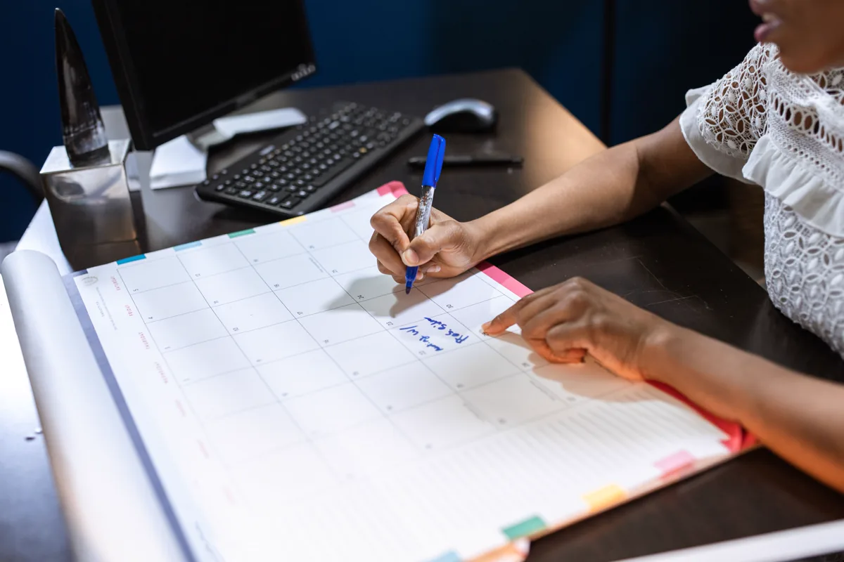 Person writing dates on a monthly calendar